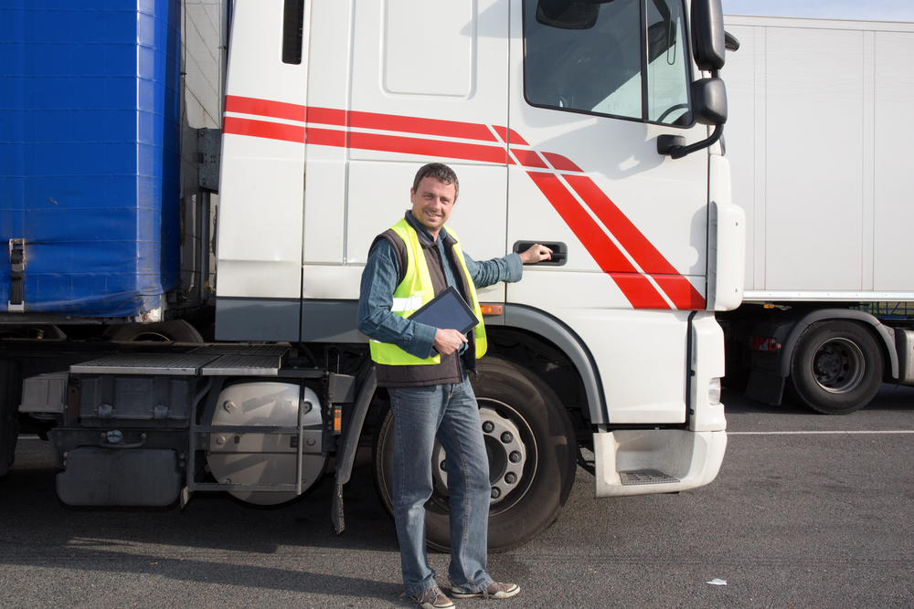 Truck driver standing by semi-truck with clipboard emphasizing fleet safety program