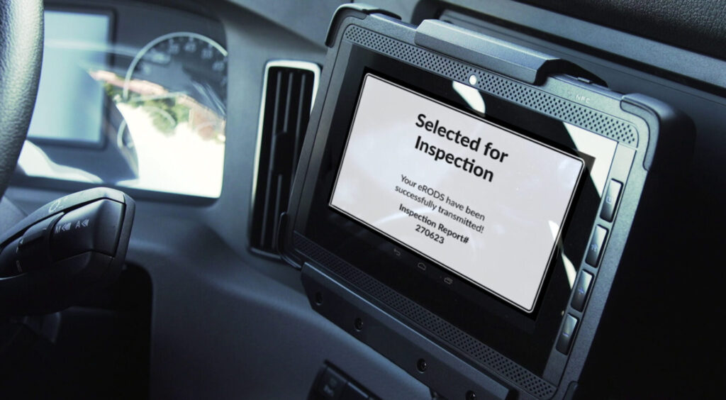 Close-up of a truck's dashboard showing an electronic display with the message "Selected for Inspection" and details about electronic records transmission.